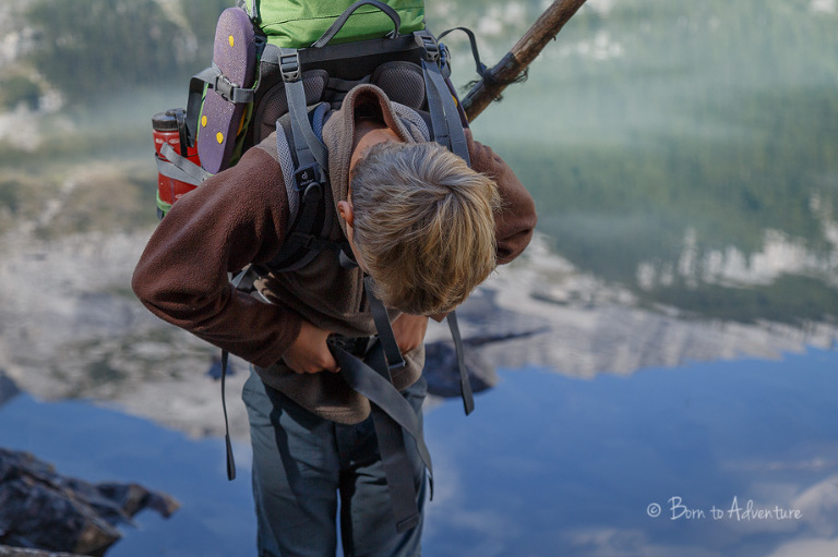 Boy adjusting his backpack with reflection in Upper Elk Lake